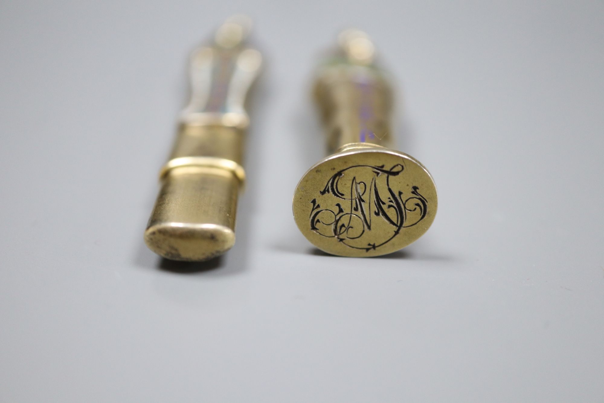An early 20th century Egyptianesque gilt white metal and enamel propelling pencil/seal, 59mm and a similar pencil case, 72mm.